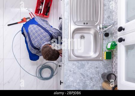 Jeune homme Nettoyage Plombier lavabo bouché dans la cuisine du tuyau Banque D'Images