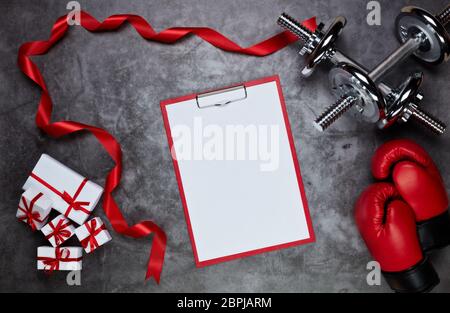 Haltères, gants de boxe, boîtes-cadeaux et tablette avec feuille vierge sur fond gris.vue du dessus. Carte de Saint-Valentin. Fitness, sport et santé Banque D'Images