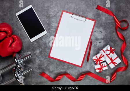 Haltères, gants de boxe, boîtes-cadeaux, tablette et tablette avec feuille vierge sur fond gris.vue du dessus. Carte de Saint-Valentin. Fitness, sport et Banque D'Images