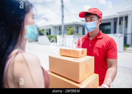 Les militaires de livraison asiatiques portent un uniforme rouge avec un capuchon rouge et un masque facial manipulant des boîtes en carton à donner à la cliente en face de la h Banque D'Images