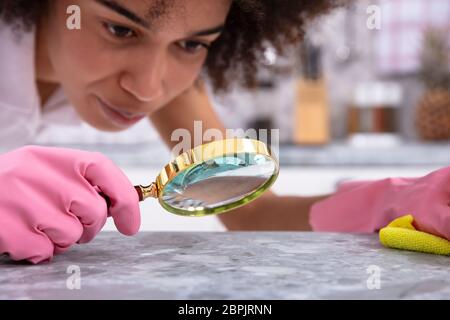 Portrait d'une jeune femme portant des gants rose à la cuisine au comptoir avec loupe Banque D'Images