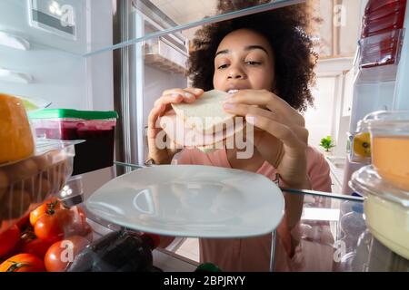 Femme de la faim en tenant la plaque sandwich de jambon frais dans le réfrigérateur Banque D'Images