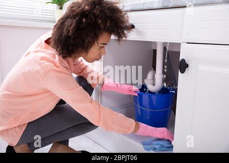 Close-up of a Young Woman Blue Bucket plaçant sous l'eau s'échappe des tuyaux de l'évier Banque D'Images