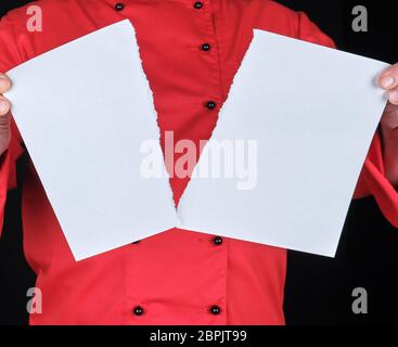 Homme dans un uniforme rouge est titulaire d'une feuille de papier blanc coupé en deux, fond noir Banque D'Images