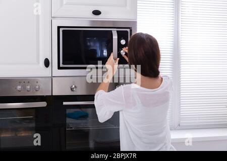 Vue latérale d'une jeune femme à l'aide d'un four micro-ondes four dans la cuisine Banque D'Images