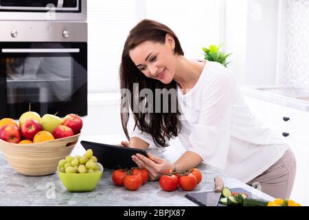 Happy Young Woman Using Digital Tablet près de légumes frais sur le comptoir de la cuisine Banque D'Images