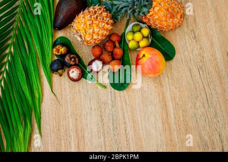 Plat Lay mélange de fruits exotiques et de feuilles de palmier sur fond brun: Ananas, avocat, mangues, mangoustan, lychee, agrumes. Un parfait endroit pour un Banque D'Images