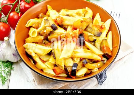 Pâtes penne à l'aubergine et les tomates dans un bol sur la serviette, la fourchette, l'ail et le persil sur une planche en bois historique Banque D'Images