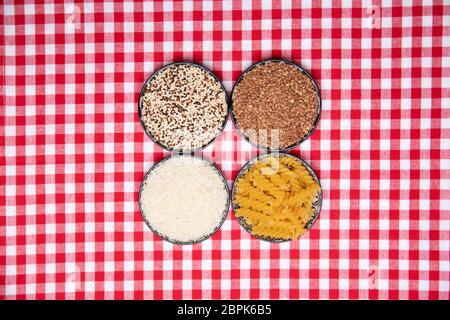 Aliments végétaux. Un cadre de quatre bols avec sarrasin, nouilles, riz et quinoa sur un nappe à carreaux rouges. Une alimentation saine. Vue de dessus avec espace pour Banque D'Images