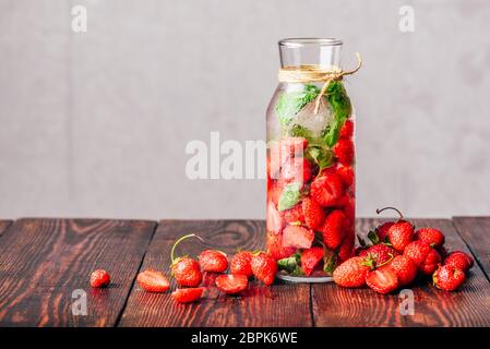 Bouteille de l'eau infusée avec des fraises fraîches et de feuilles de basilic.éparpillés sur les baies de table en bois. Banque D'Images