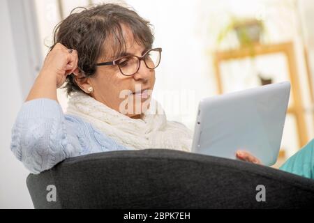 Charmante brunette senior femme avec des lunettes à l'aide d'une tablette numérique à la maison Banque D'Images