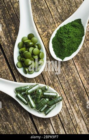 La chlorelle vert comprimés ou l'orge en pilules et en poudre dans une cuillère en céramique. Banque D'Images