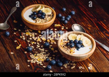 Avec Granola banane, myrtille et du yaourt grec pour le petit-déjeuner. Ingrédients éparpillés sur la table en bois. Banque D'Images