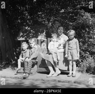 Années 1960, histoire, été et une mère assise à l'extérieur dans le jardin avec ses cinq enfants posant pour une photo de famille, Angleterre, Royaume-Uni. Banque D'Images