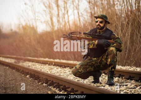 Le soldat de l'armée en uniforme militaire avec arme à arbalète est sur la voie ferrée à l'extérieur. Banque D'Images