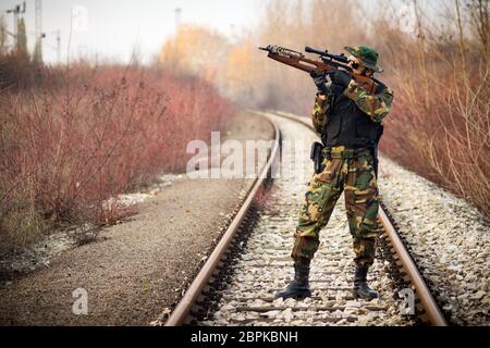 Le chasseur ou le soldat en uniforme militaire est tiré avec une arme à arbalète et debout à l'extérieur sur la voie ferrée. Banque D'Images