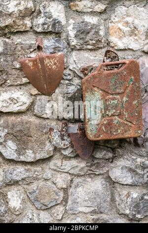Vieille essence rouillés en décomposition canister et tête pelle attaché à un mur d'un bâtiment dans une campagne Banque D'Images