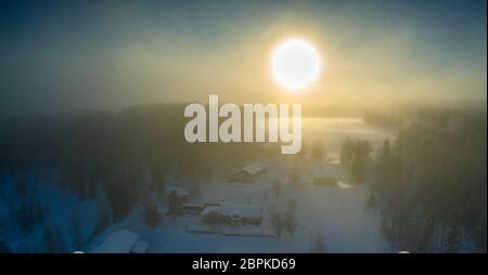 Vue majestueuse du coucher de soleil d'hiver avec très grand point de soleil dans l'air brumeux gelé, forêt de pins d'hiver, aérienne, village de Grano, autour de la ville d'Umea Banque D'Images