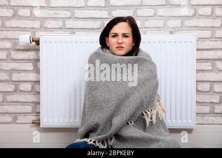 Jeune femme enveloppée dans une couverture assis près de Radiateur à Accueil Banque D'Images