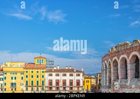 Les murs en calcaire de l'arène de Vérone avec fenêtres à arche et anciens bâtiments multicolores colorés de la place Piazza Bra dans le centre historique de Vérone, fond bleu ciel, région de Vénétie, Italie du Nord Banque D'Images