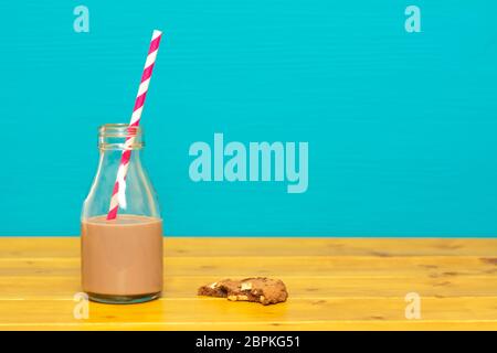 Un tiers de pinte de lait en verre bouteille à moitié pleine du chocolat avec avec une paille rétro et une demi-biscuit aux brisures de chocolat mangé, sur une table en bois nouveau Banque D'Images