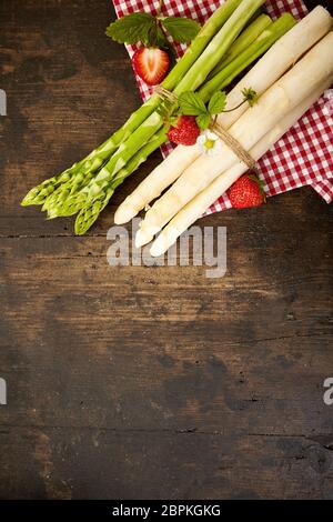 Deux lots de matières premières fraîches asperges vertes et blanches liés avec de la ficelle sur un chiffon rouge et blanc sur bois rustique with copy space Banque D'Images