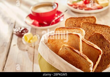 Toasts croquants fraîchement préparés, servis dans un sac en tissu avec le café et le beurre en arrière-plan flou sur table en bois Banque D'Images