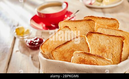 Toasts de pain blanc frais pour le petit-déjeuner, servi dans sac en tissu avec beurre, confiture et tasse de café en arrière-plan flou Banque D'Images