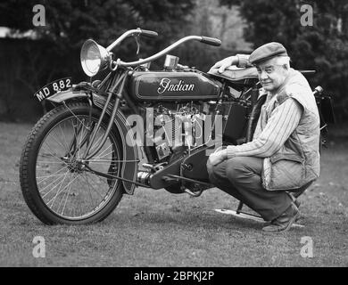 Années 1980, un homme mûr s'agenouillant à côté de sa moto scoute « indienne » restaurée, la première moto américaine. Fondée à l'origine pour fabriquer des bicyclettes, la Hendee Manufacturing Comany a produit en 1901 deux unités de production de la moto indienne et en 1905, Oscar Hedstrom, cofondateur de l'Inde, a établi le record mondial de vitesse de la moto de 56 mph. La moto « Indian Scout » a été introduite dans les années 1920 et a été construite jusqu'en 1949, devenant un modèle populaire. L'entreprise a fait faillite en 1953, mais les anciens modèles sont très recherchés et collectables. Banque D'Images