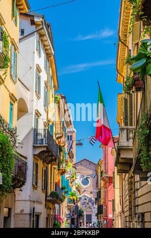 Rue italienne typique avec des bâtiments traditionnels colorés avec des fenêtres à volets, des balcons de plantes et de drapeau, église Basilica di Santa Anastasia, centre historique de la ville de Vérone, région de Vénétie, Italie Banque D'Images