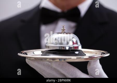 La mi-section de Waiter's Hand Holding Service Bell dans la plaque Banque D'Images