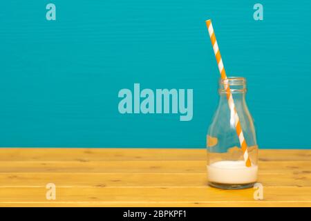 Un tiers de pinte de lait en verre bouteille avec racaille du lait crémeux frais avec une paille papier rétro, sur une table de bois contre un arrière-plan bleu sarcelle Banque D'Images