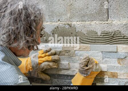 Travailleur manuel avec des gants de protection en pressant les carreaux ornementaux dans une colle sur un mur. Banque D'Images