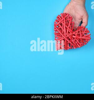 Coeur en bois rouge en osier dans une main féminine sur un fond bleu, copy space Banque D'Images