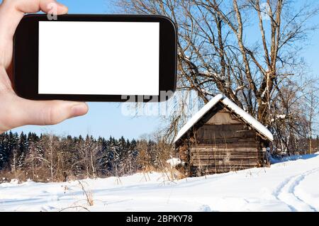 Concept de voyage - photographies de tourisme ancienne cabane en bois près de la forêt dans la journée d'hiver ensoleillée de little village en Russie sur smartphone Avec cut ou Banque D'Images