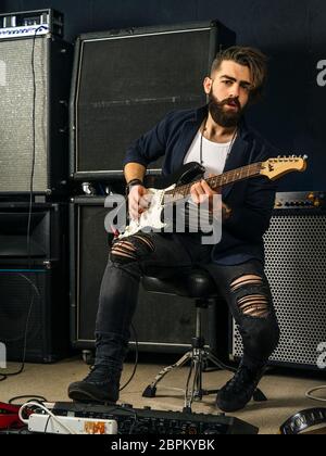 Photo d'un homme à barbe assis et jouant de sa guitare électrique dans un studio d'enregistrement. Banque D'Images