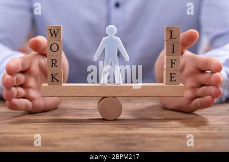 La figure humaine se tenant entre le travail et la vie des blocs de bois sur Seesaw protégée par une femme d'affaires Banque D'Images