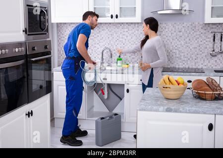 Femme se plaignant d'encrasser lavabo pour jeune homme plombier dans Cuisine Banque D'Images