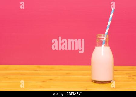 Lait frappé aux fraises avec une paille papier rétro dans une troisième pinte de lait, bouteille en verre sur une table en bois contre un fond rose Banque D'Images