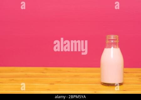 Lait frappé aux fraises dans un tiers de pinte de lait, bouteille en verre sur une table en bois contre un arrière-plan peint rose Banque D'Images