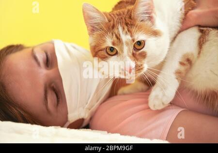 Jeune femme en tissu blanc virus masque de visage jouant avec son chat, détail sur les yeux félins, propriétaire flou en arrière-plan Banque D'Images