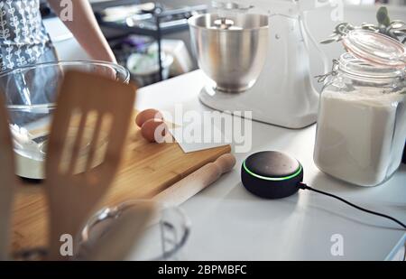 Enceinte Smart Home répondant à une femme dans la cuisine tout en faisant cuire dans un présentoir verrouillé Banque D'Images