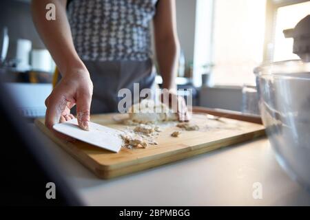 Femme utilisant un grattoir à pâte, faisant de la pâte fraîche à la maison dans sa cuisine. Banque D'Images