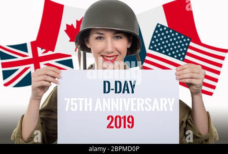 Souriante jeune femme habillé en uniforme militaire de la seconde guerre mondiale montrant casque avec pancarte à d-day anniversaire Banque D'Images