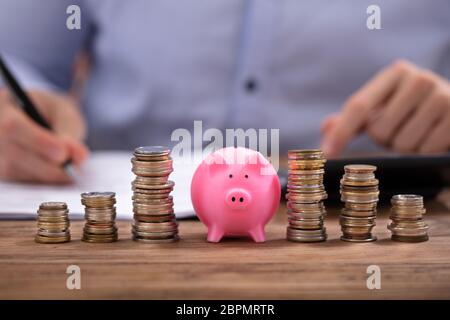 Pièces empilées et Pink Piggy Bank dans le calcul de facture sur un bureau en bois Banque D'Images
