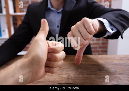 Deux personnes Showing Thumbs Up et signe de pouce vers le bas In Office Banque D'Images
