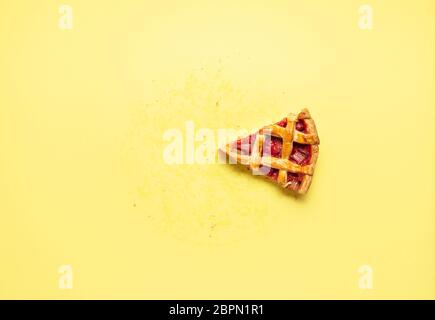 Une seule tranche de tarte aux fraises au rhubarbe avec une croûte de treillis sur fond jaune. Disposez à plat avec le dernier morceau de gâteau, les traces de graisse et les miettes Banque D'Images
