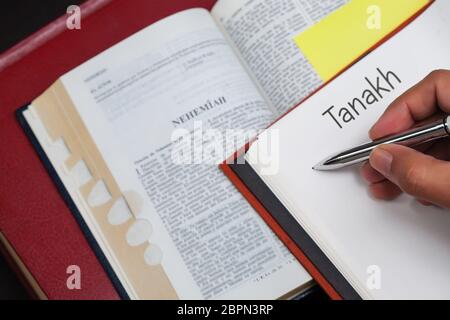 Un étudiant de Tanakh écrit sur un carnet avec une bible ouverte au livre du prophète Néhémie. Banque D'Images