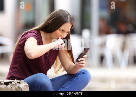 Femme en colère mauvaise réception de contenus en ligne dans un téléphone mobile assis dans un banc dans la rue Banque D'Images