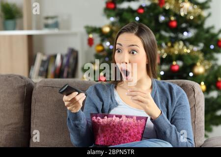 Surpris femme regardant la télévision en vacances de Noël assis sur un canapé dans la salle de séjour à la maison Banque D'Images